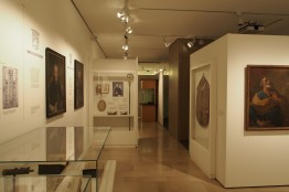 Blick in die Ausstellung: mehrere Gemälde, ein Bischofsstab und eine Glasvitrine sind zu sehen.