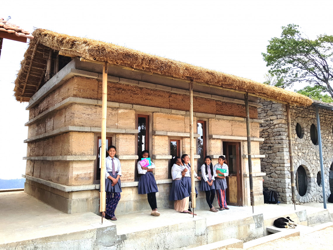 5 Mädchen mit Schulheften in der Hand stehen vor einem Holzhaus