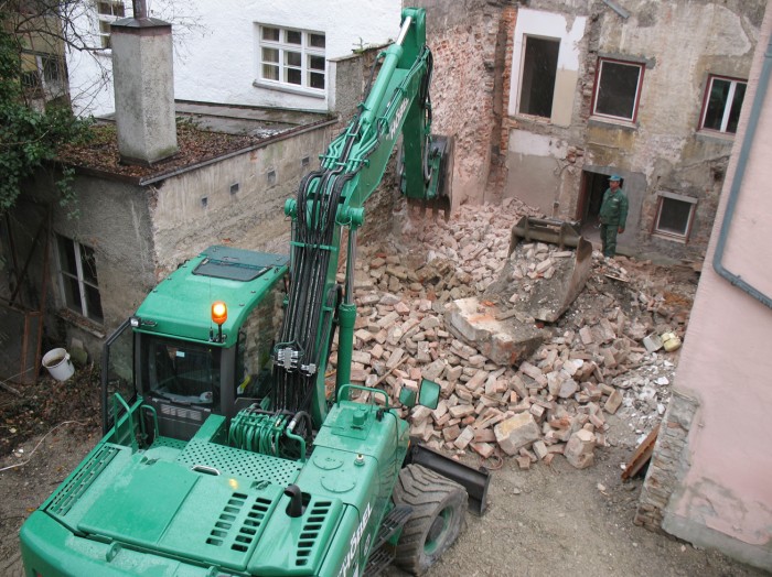 Ein grüner Bagger reißt die Mauer eines Hauses, an dessen Stelle der Museumsneubau entstehen soll, ein.