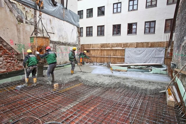 Die Decke über dem Kellergeschoss wird betoniert, zwei Arbeiter gießen den Beton auf das vorbereitete Gitter aus Baustahl, zwei Arbeiter verteilen den Beton gleichmäßig.