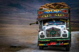Ein bunter, schwer mit S&auml;cken beladener Bus auf einer Stra&szlig;e in karger, nebliger Landschaft.