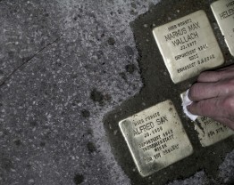 Eine Hand putzt mit einem Tuch mehrere Stolpersteine.