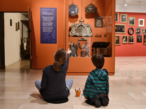 zwei Kinder sitzend auf dem Boden sehen sich Exponate in einer Vitrine der Sonderausstellung &quot;Wunschkonzert&quot; an 