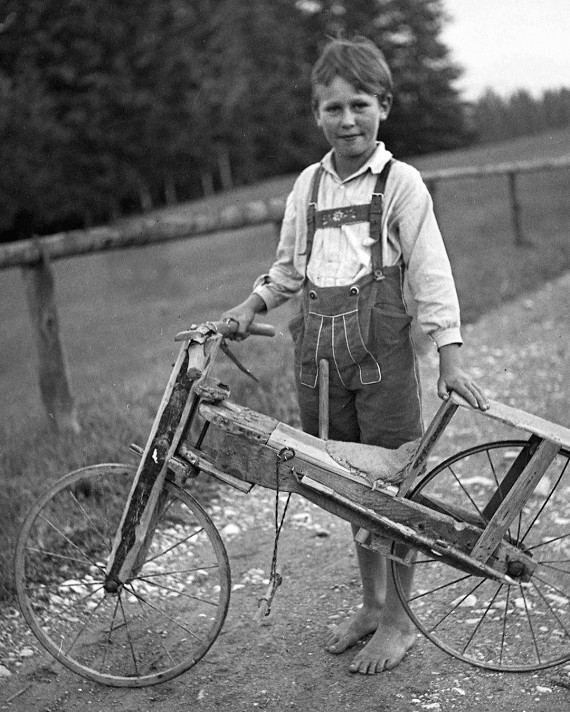 Schwarzweiße Fotoaufnahme, die einen Jungen mit einem selbstgebauten Fahrrad zeigt.